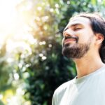 Model closing his eyes and breathing deeply, surrounded by trees