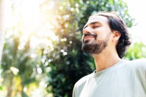 Model closing his eyes and breathing deeply, surrounded by trees